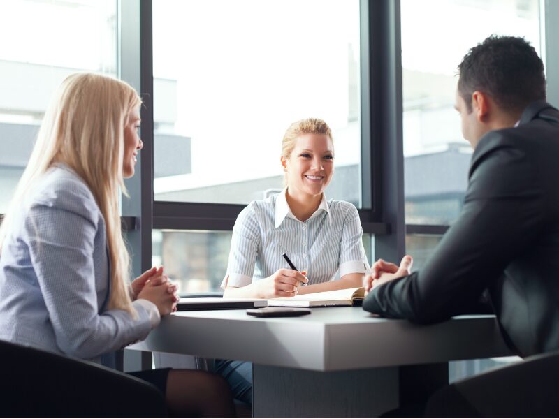 A man and a woman sit across a woman in a professional setting, a client meeting or consultation between a lending expert or lender and business owners seeking overdrafts