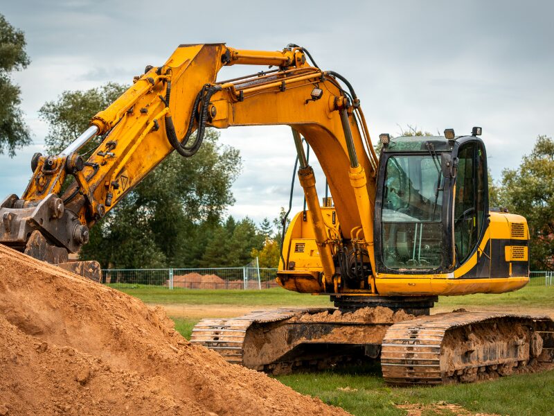 A small yellow excavator driving over grass and hauling dirt from a small pile