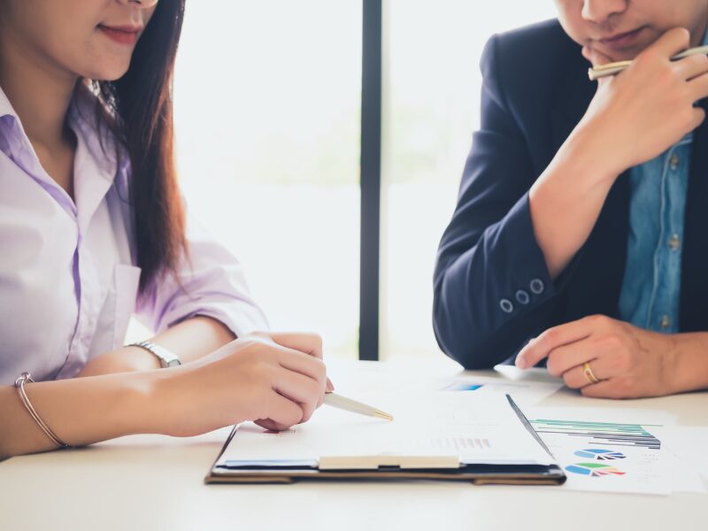 Cropped photo of a woman discussing a document on a clipboard to a man with his hand on his chin, A financial expert discusses fixed vs variable interest-only loan to a borrower