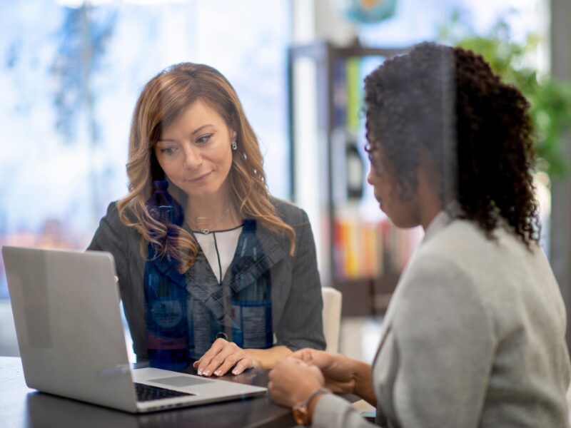 Two women discussing interest-only loan options, an investor discussing options with a lender or financial expert, photo taken from behind a glass wall or door