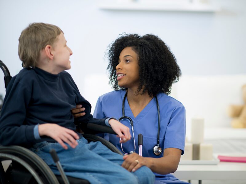 A healthcare worker addresses and talks to a child with a disability sitting in a wheelchair