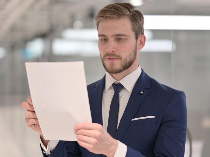 A man in a suit holds up and reads a document, reading refinancing options for his caveat loan
