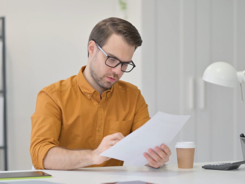 A man in glasses intently reads a document while sitting behind a desk, contemplating exit strategies for his caveat loan