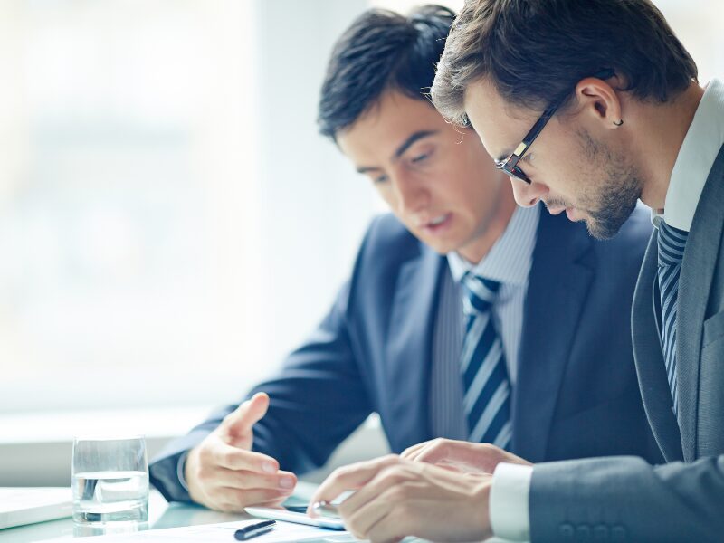 Two men in suits in a professional setting having a serious discussion while looking at documents, business owners discussing their caveat loan exit strategy