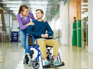 Healthcare worker or disability support worker holds the shoulders of a man on a wheelchair and smiles, man with disability smiling
