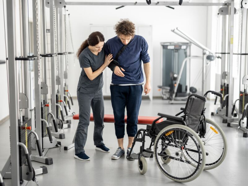 An NDIS provider or healthcare worker assists a man with injuries or disabilities during physical therapy