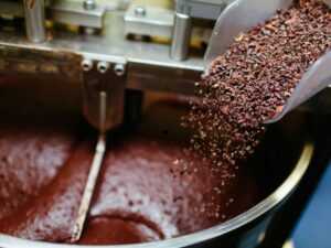 Cacao nibs being poured into a large chocolate mixer, food manufacturing equipment for industrial food production