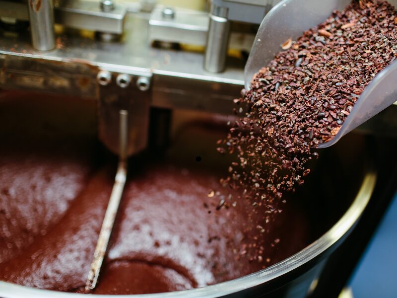 Cacao nibs being poured into a large chocolate mixer, food manufacturing equipment for industrial food production