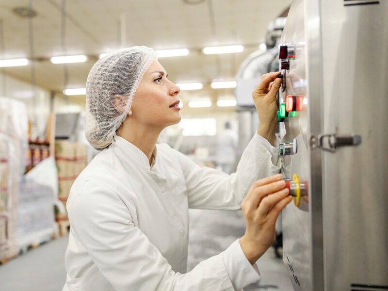 A woman in sanitary clothing operates an industrial food processing machine