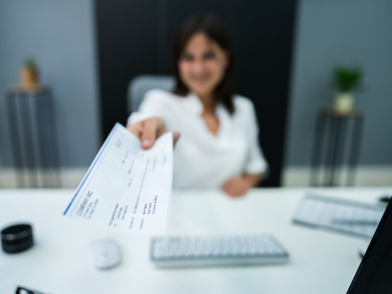A woman holding forward a payslip, depth of field photo with the woman blurred and the payslip in focus