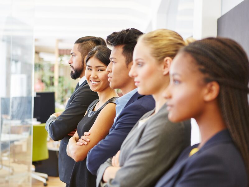 The staff of a small business line up with their arms crossed, looking into the distance, while one of them smiles directly at the camera