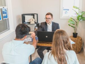 A man seated next to a woman shakes the hand of a mortgage broker, who is sitting across both of them, clients agreeing to a loan solution