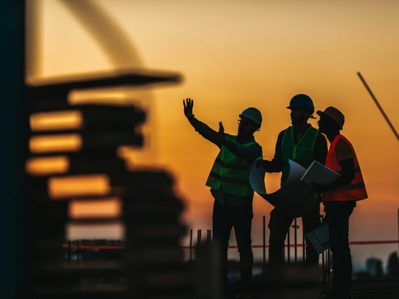 Construction workers, engineers, or developers wearing safety gear assess an ongoing construction site during sunset