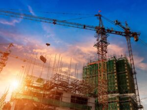 The sun sets behind a large construction project, ongoing construction on a building with visible rebar and large cranes operating