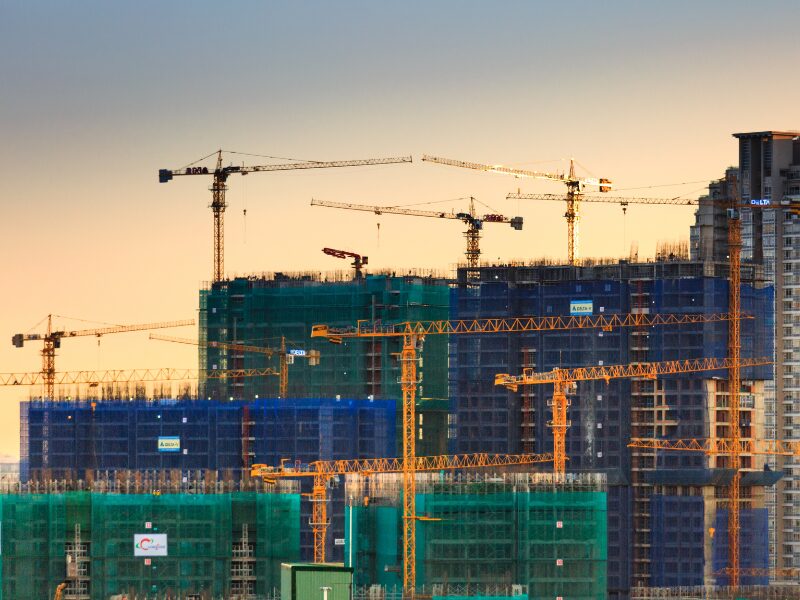 A large multi-building ongoing construction project, with visible bare concrete, rebar, and large cranes working on the buildings