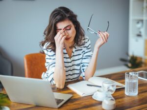 A woman takes off her glasses and massages her forehead, stressed NDIS provider with ATO tax debts