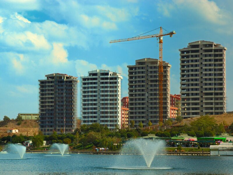 Four buildings in a property development project under construction, with a large body of water in front with fountain water features