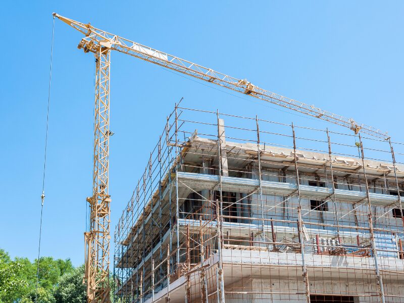 An ongoing construction project, low-rise building under construction, large crane operating on the project