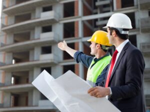 Property developers in hard hats examine an ongoing development project while holding blueprints