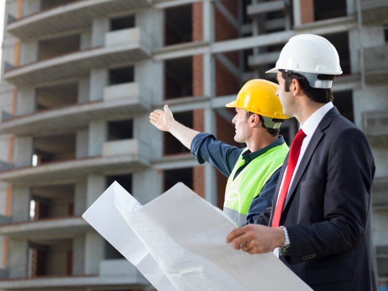 Property developers in hard hats examine an ongoing development project while holding blueprints
