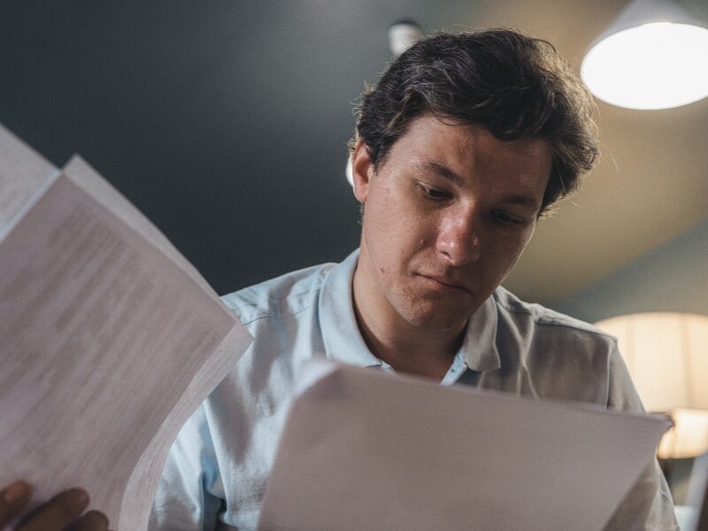 A man with a slightly tense expression reads documents, a business owner calculating and reading GIC on his tax debt