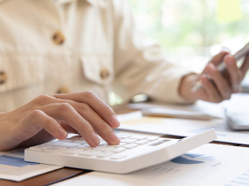 Cropped photo of a person using their smartphone and a calculator at the same time, a business owner calculating GIC