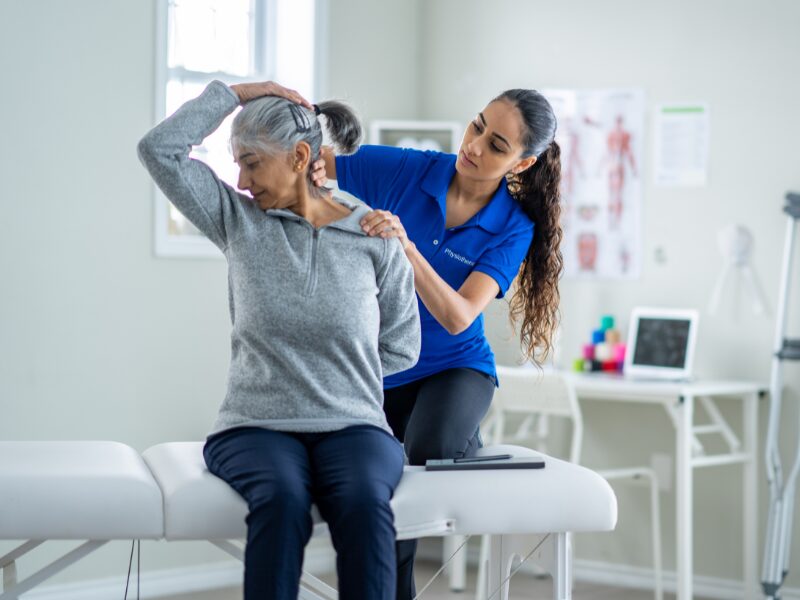 A physiotherapist assists their client with neck stretches