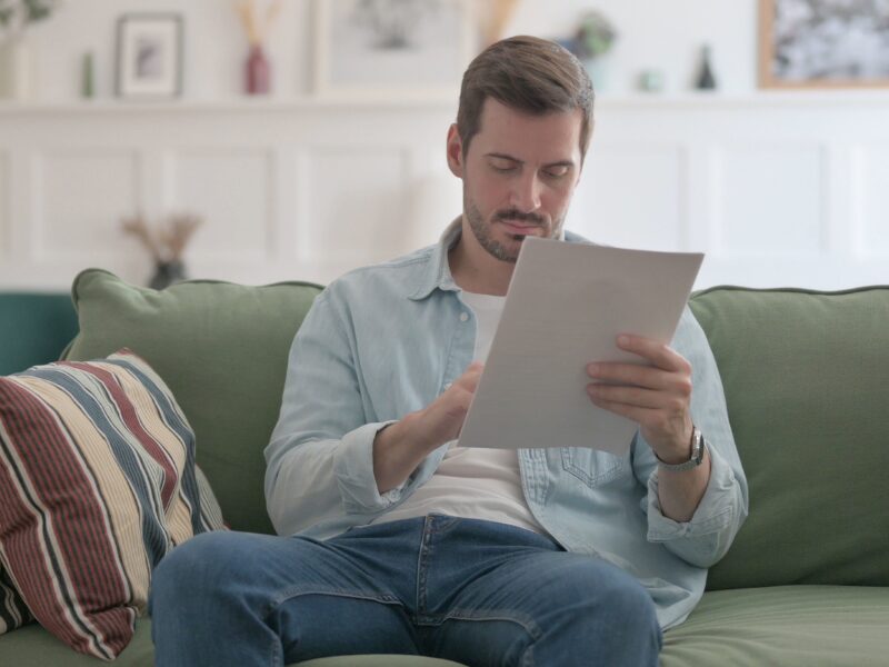 A man reads a document as he sits on his couch, man reading the new changes in tax debt interest rate deductibility