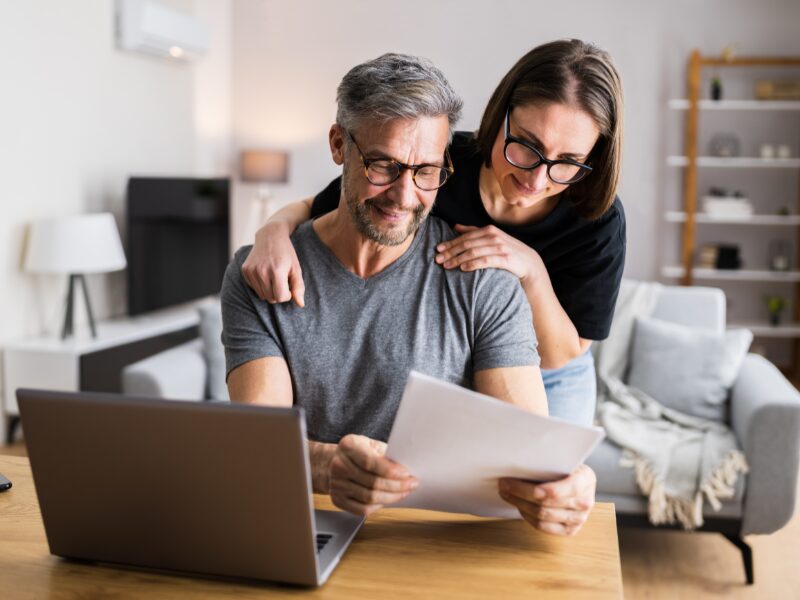 A couple smiles as they read a document together, the couple finding solutions for their tax debt, including tax debt loans