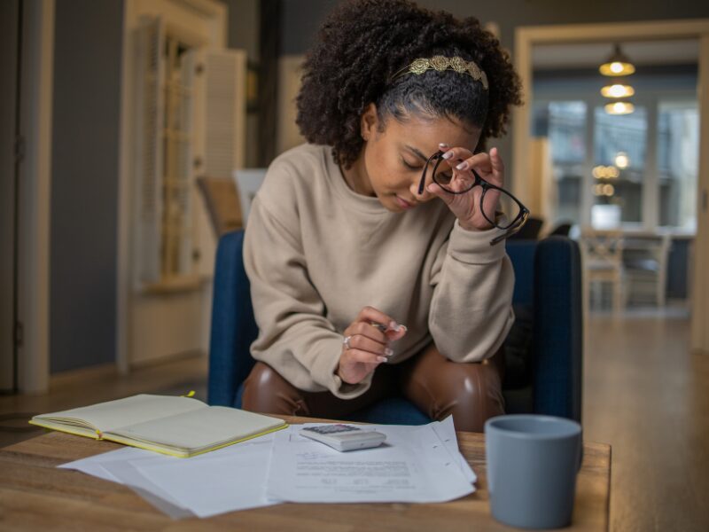 A woman removes her glasses in stress as she calculates the interest on her tax debts to the ATO