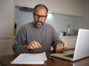 A man holding a calculator looks at a document on the table, a man calculating tax debts with non-deductible interest charges