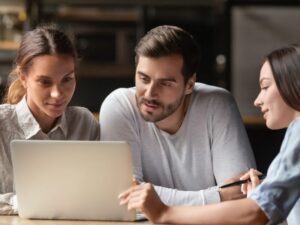 A mortgage broker or lender shows a laptop to two business owners, looking at types of tax debt loans available in Australia