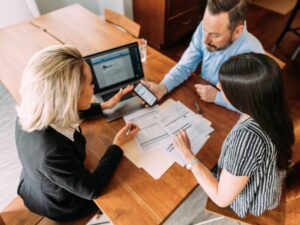Three financial planners in a discussion while one holds out his smartphone, a laptop and several documents seen on the table