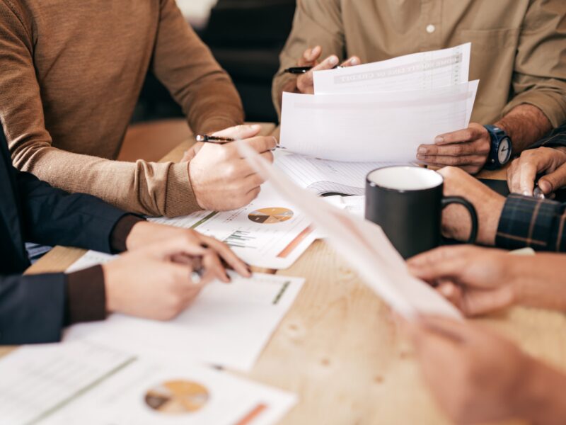 Cropped photo of a group of five financial planners in a work discussion, looking at several financial documents