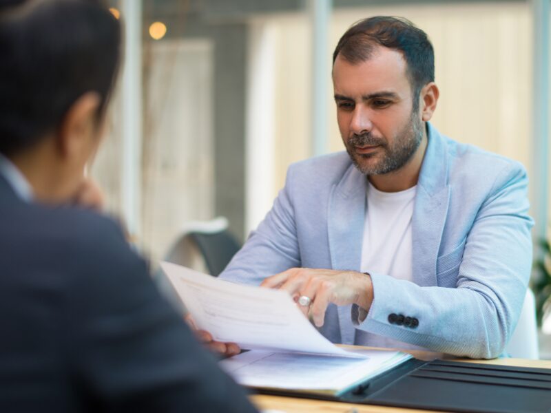 A business owner discussing tax debt solutions with a loan broker or lender, a man holding a document while in discussion with another man in a professional setting