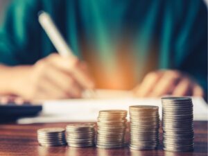 Piles of coins in ascending order, a person writing on paper in the background, concept photo for making extra repayments on a loan