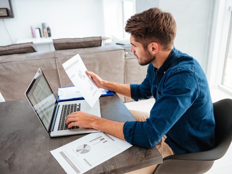 A man using his laptop while looking at a document, a home buyer deciding on what repayment schedule to choose