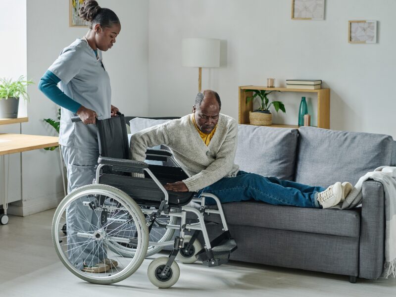 A disability support worker helps an elderly client get into a wheelchair