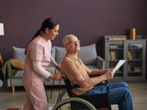 A disability support worker talking to a patient while she pushes his wheelchair, the patient holding a document, a happy conversation between a carer and an elderly man