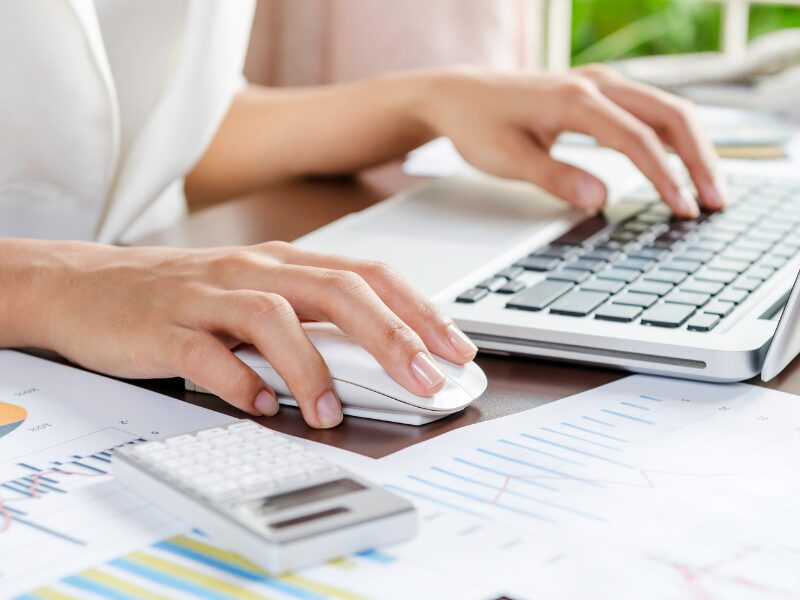 A person uses their laptop, documents and a calculator on the table, a business owner preparing for ATO policy changes