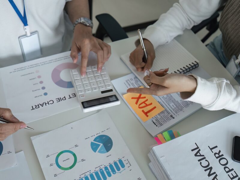 Two people calculating the impact of tax interest deductibility changes, people in a discussion surrounded by documents labelled “tax” on a sticky note
