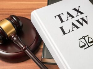 A large white book with the text “Tax Law” and a law scales symbol piled on top of a grey book next to a judge’s gavel