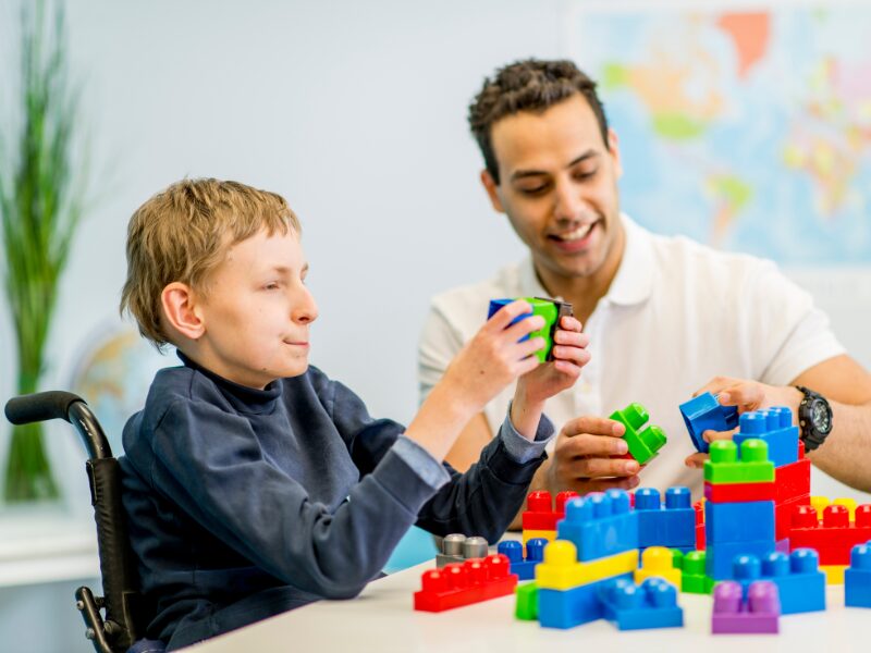 A disability support worker plays with toy blocks with a child in a wheelchair