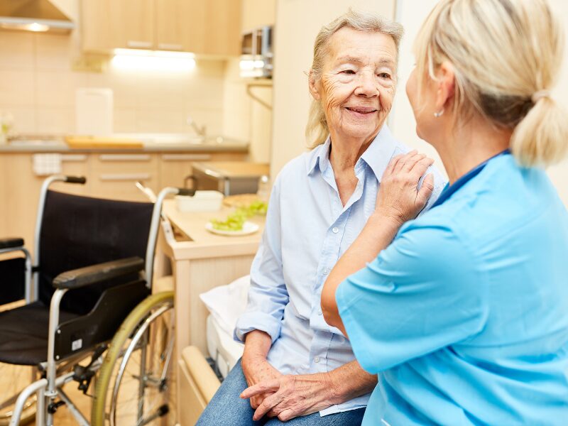 A disability support worker places a reassuring hand on the shoulder of an elderly woman