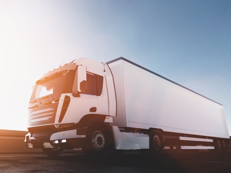 A white freight truck driving down the road with a light flare in the background