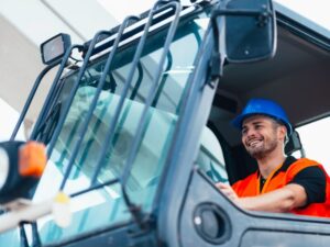 A construction operator in protective gear smiles as he drives large equipment for construction