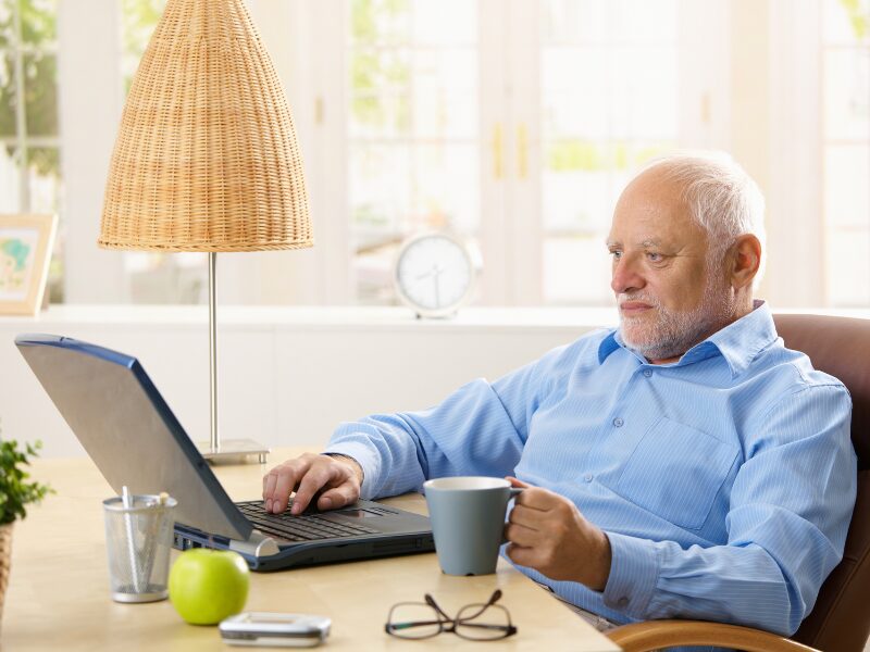 A business owner uses his laptop while holding a cup of coffee, business owner looking for strategic solutions before the ATO bans interest deductibility