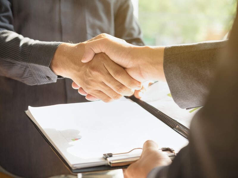 Cropped photo of two people shaking hands while one presents the other with documents
