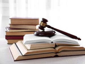 A judge’s gavel on top of a pile of open books with a pile of closed books in the background