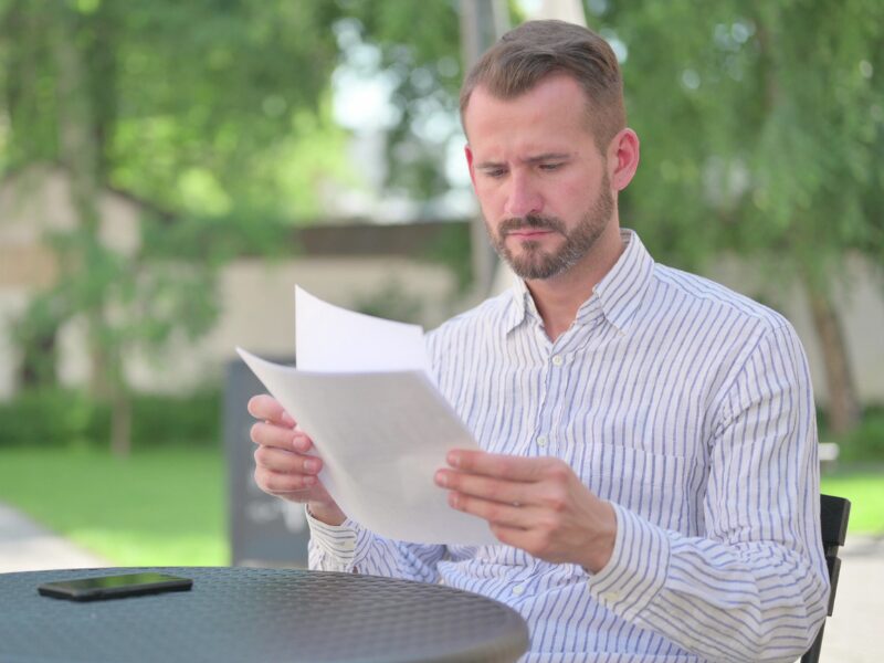 A man sitting at a table outdoors reading documents, reading details about the tax interest deductibility changes